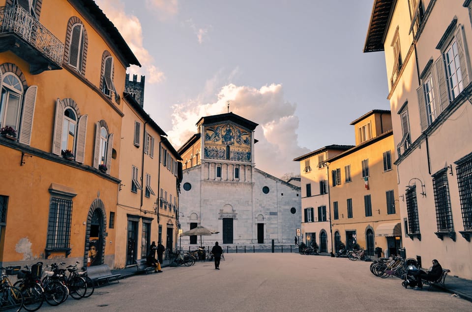 Evening light on a piazza with bicycles, and a white church facade with a golden mosaic above the door