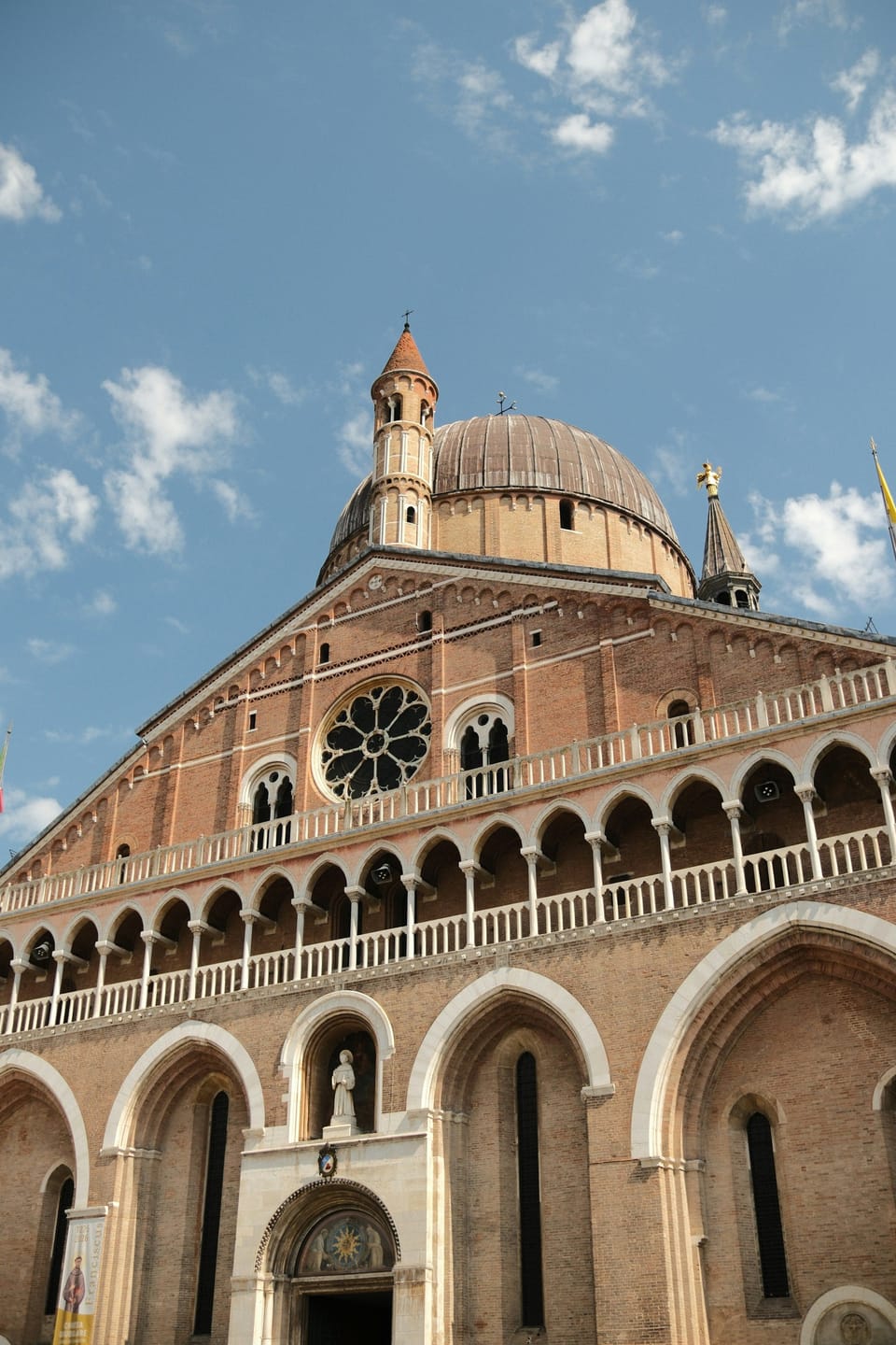 Brick facade of a basilica with a rose window and Byzantine domes under a blue sky